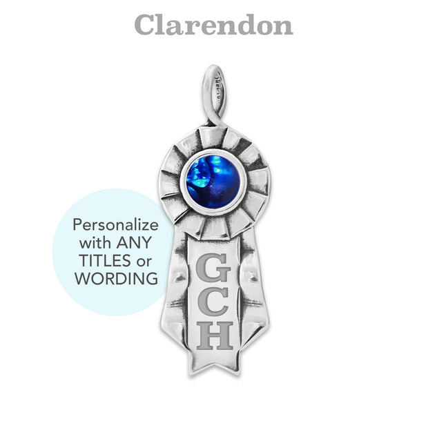 Silver ribbon pendant with blue cabochon and 'GCH' engraving on a white background, featuring the font 'Clarendon'.