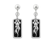 A pair of sterling silver earrings featuring a paw print design with flames shooting off it, attached to a rectangular black background.
